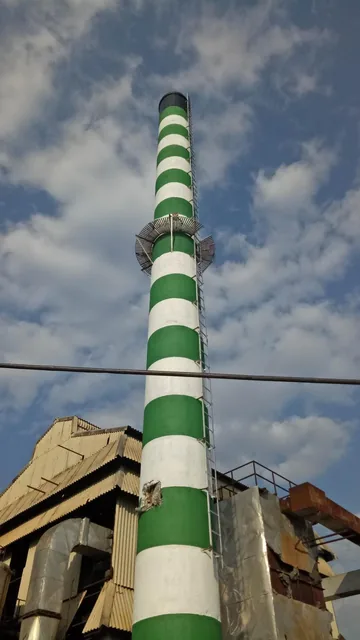 Green-and-white RCC chimney with an external ladder against a cloudy sky.