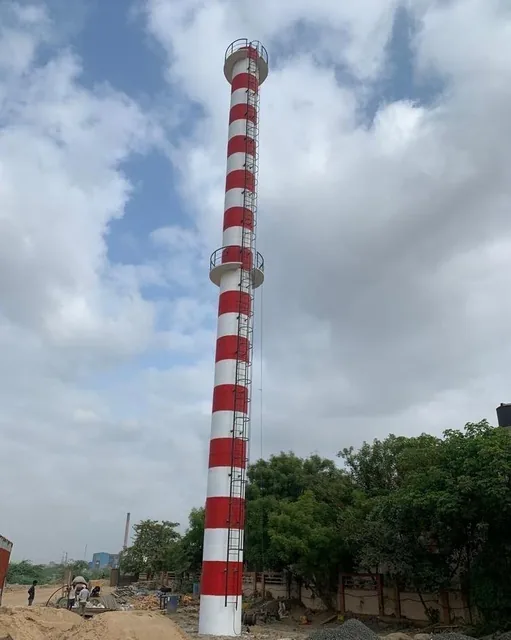 Red-and-white chimney with access platforms beside trees.